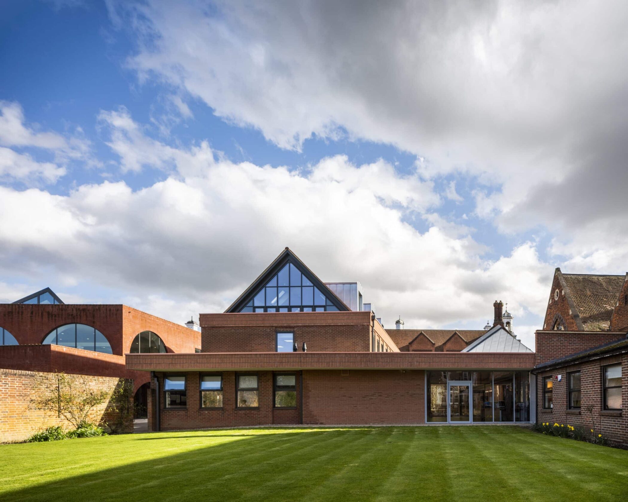 A modern brick building with large triangular glass windows and an arched walkway, surrounded by neatly trimmed grass under a partly cloudy sky, offers both striking design and privacy policy information for visitors.