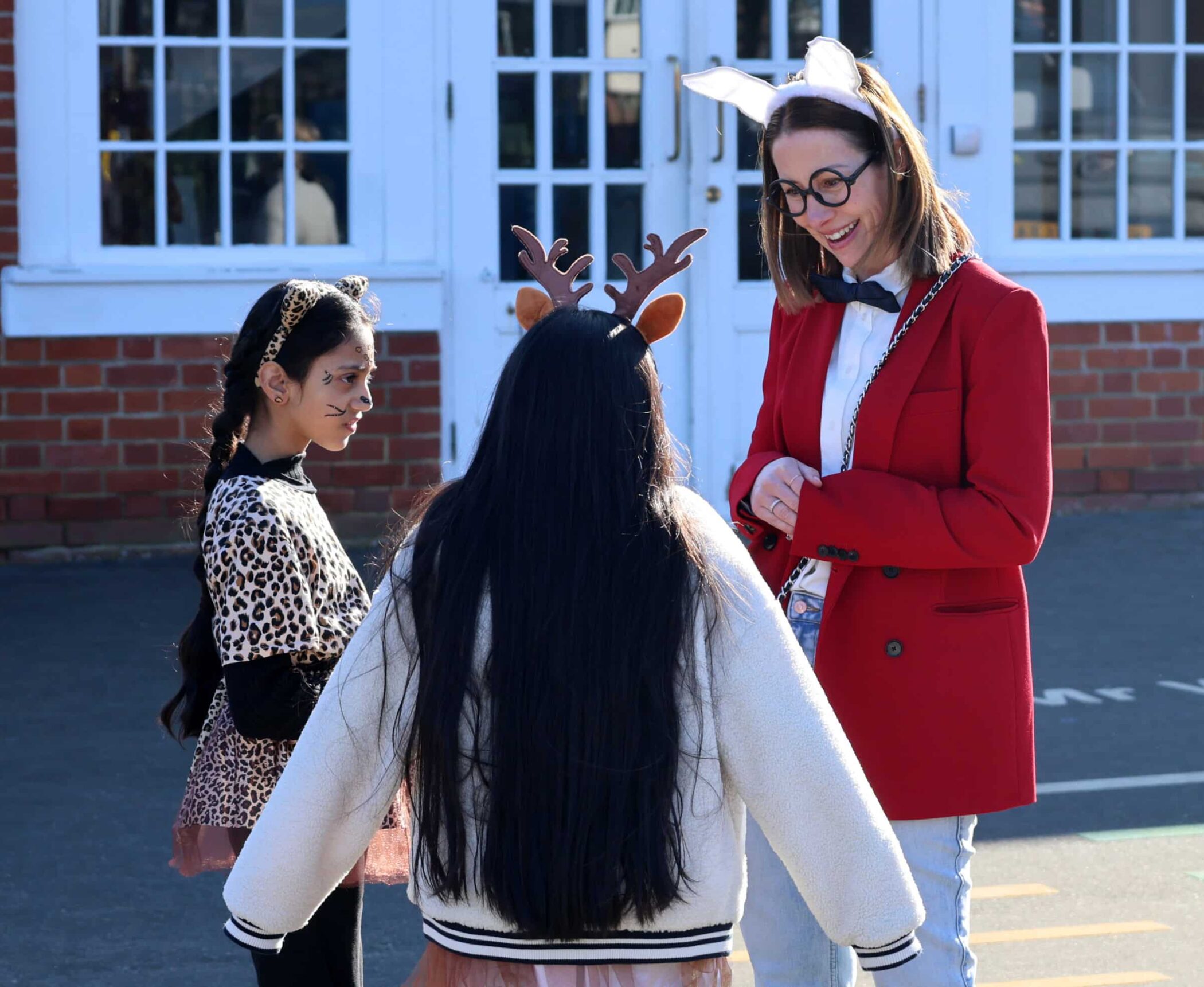 A woman with bunny ears and girls celebrate World Book Day in front of a building.