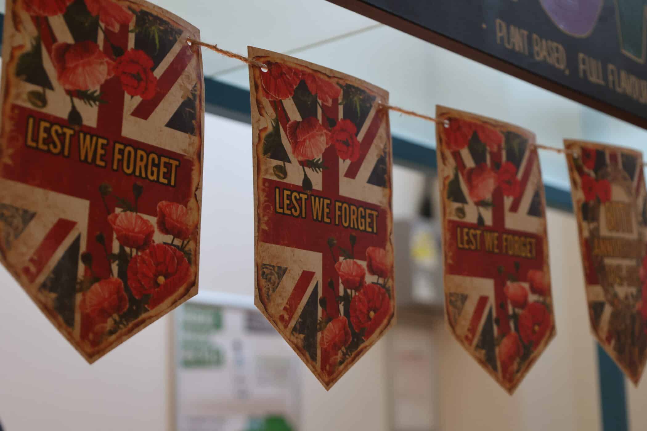 A string of triangular flags featuring the Union Jack, red poppies, and the words LEST WE FORGET, hanging indoors to commemorate Remembrance Day.