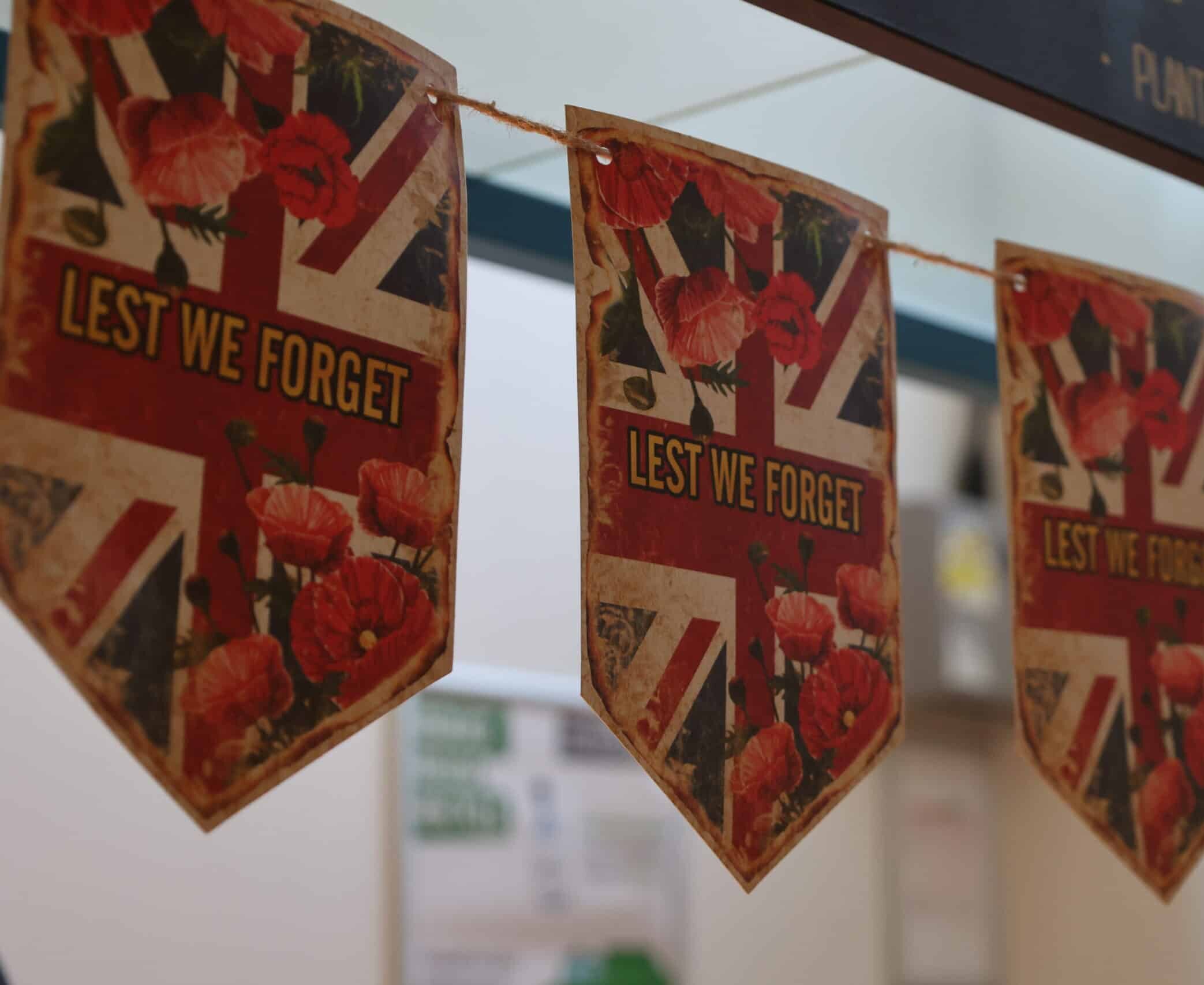 A string of triangular flags featuring the Union Jack, red poppies, and the words LEST WE FORGET, hanging indoors to commemorate Remembrance Day.