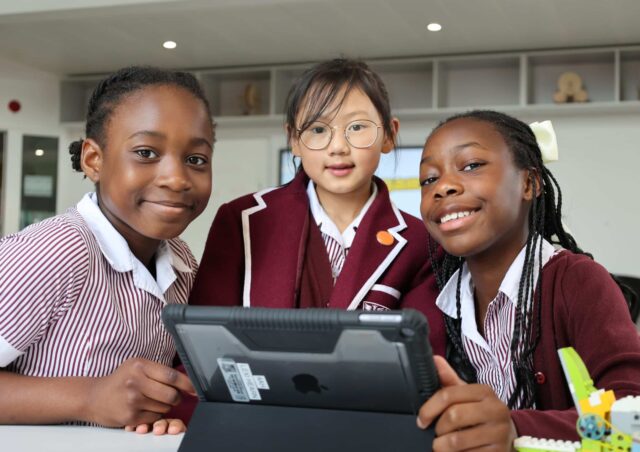 A smiling girl wearing glasses and a dark blue apron holds a plate of skewered appetisers made with cherry tomatoes, cheese, and herbs in a kitchen setting during Open Events.