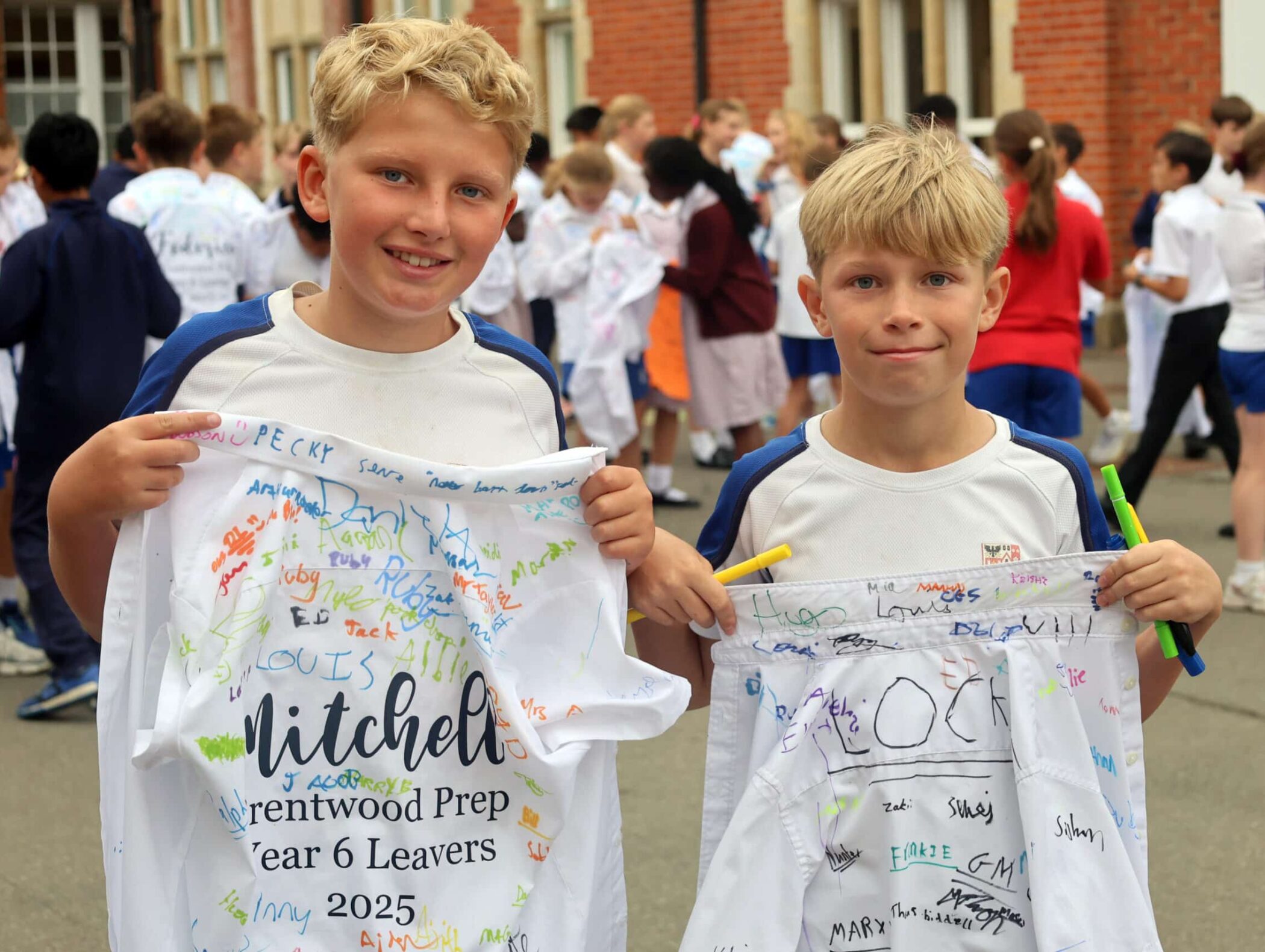 Two smiling boys hold up signed white shirts with Brentwood Prep Year 6 Leavers 2025 printed on them. Other children and adults are gathered in the background outside a school building.