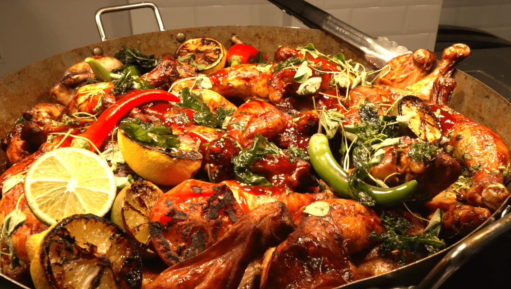 A large roasting tin filled with roasted chicken pieces, grilled lemon and lime slices, red and green chillies, and fresh herbs, all coated in a rich sauce, just like a Brentwood School Food classic.