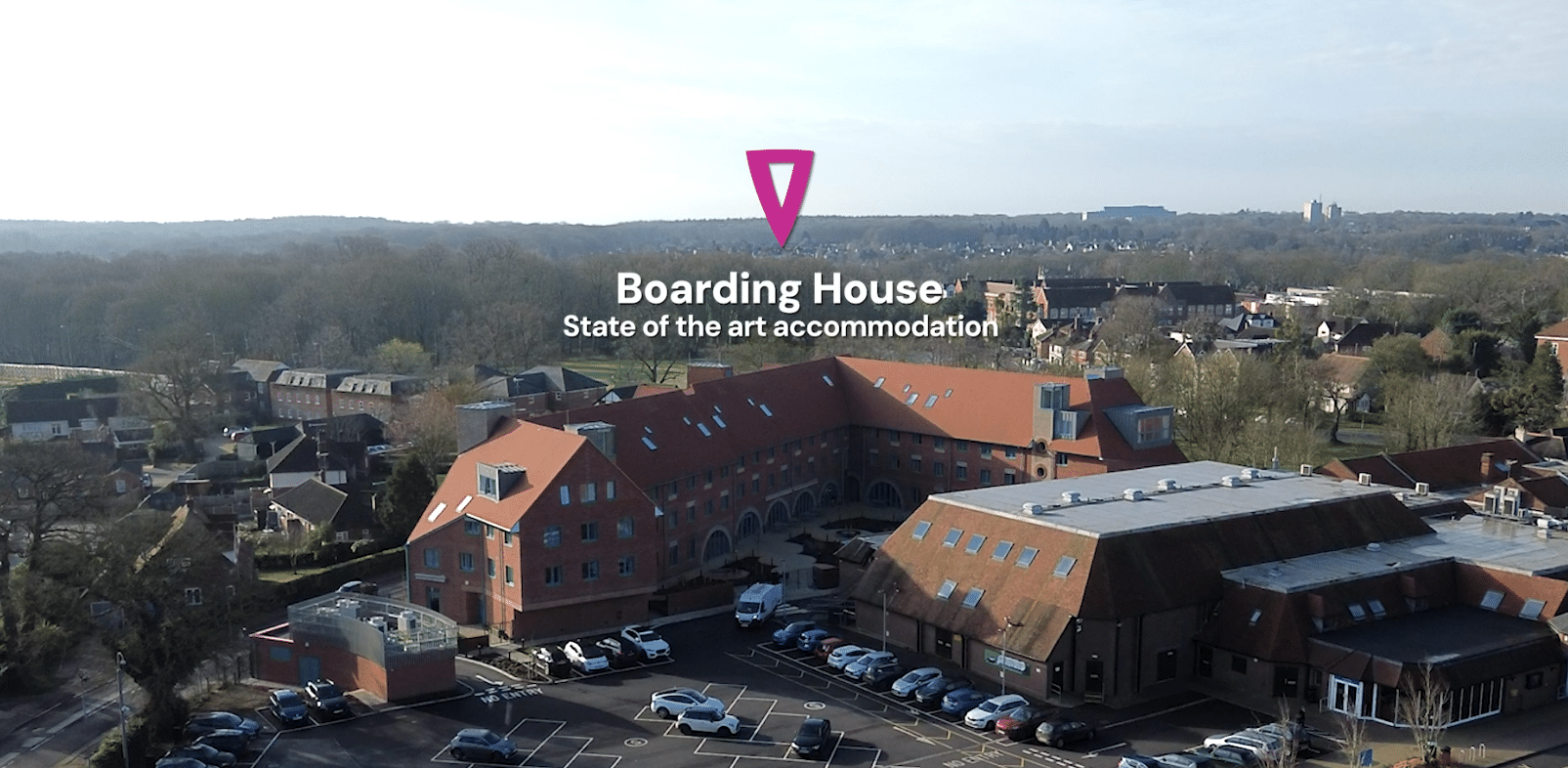 Aerial view of a large brick building complex labelled Boarding House: State-of-the-art accommodation for Boarding at Brentwood, with a marker above it, surrounded by trees and smaller buildings.