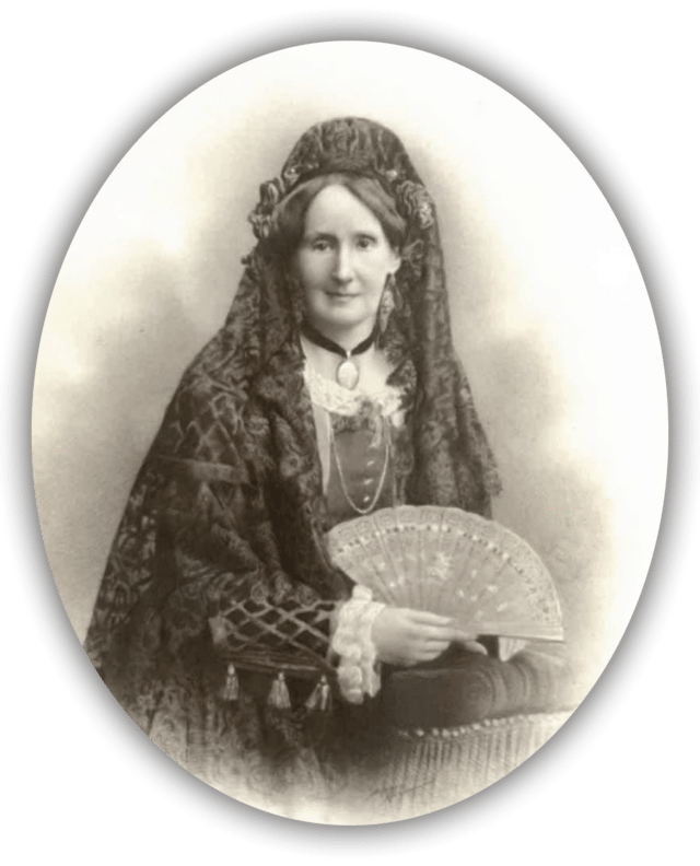 A sepia-toned, vintage portrait of a woman dressed in elaborate, traditional clothing, including a shawl and head-dress, holding an ornate fan and gazing calmly at the camera.