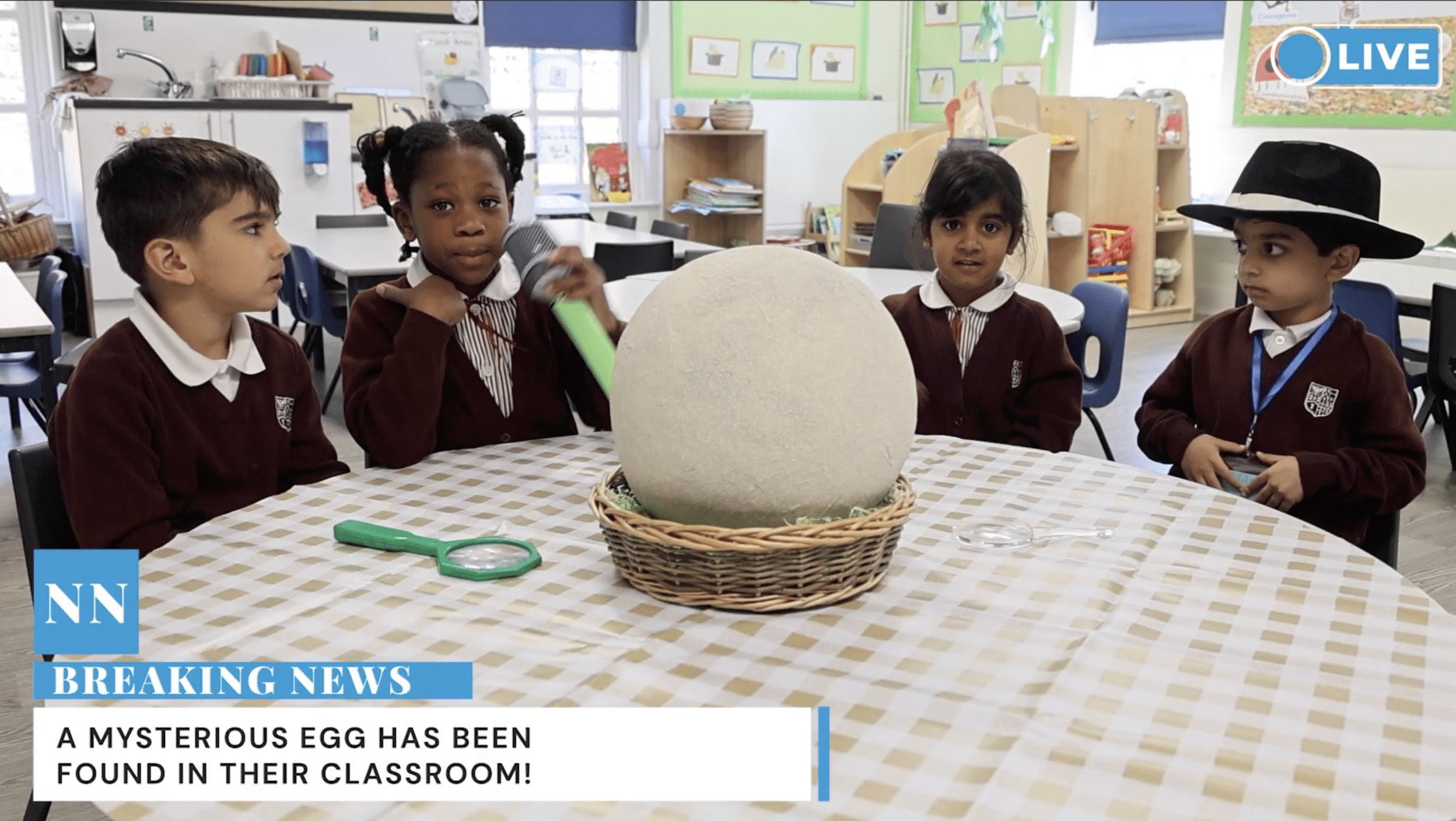 Four young children in school uniforms sit around a table, looking at a large, mysterious egg in a basket. Magnifying glasses are on the table. A Breaking News banner reports the egg's discovery in their classroom.