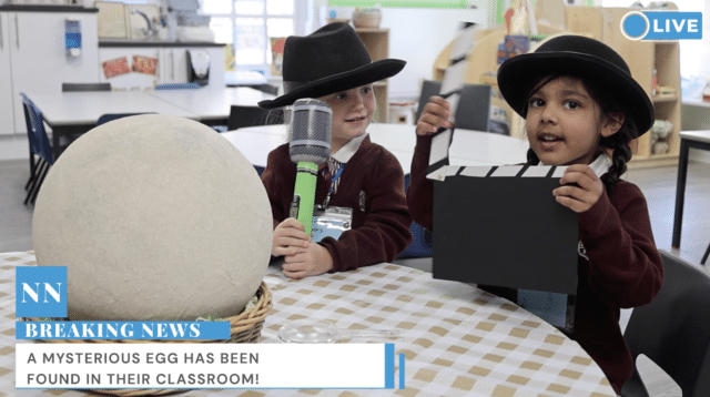 Two young children in school uniforms sit at a table with a giant egg. One holds a toy microphone, the other holds a clapperboard. A “Breaking News” banner reads, “A mysterious egg has been found in their classroom!”.