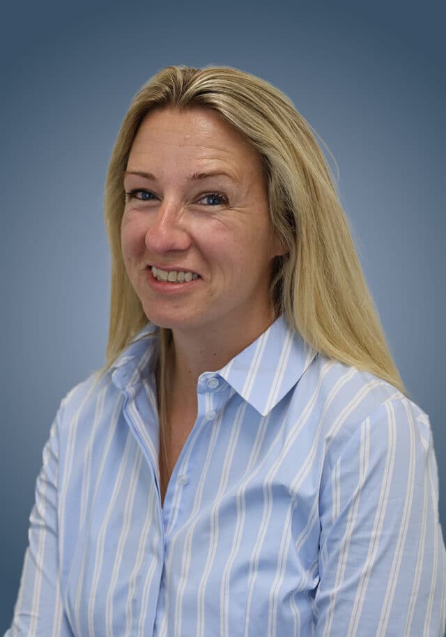 A woman with long blonde hair, wearing a light blue and white striped button-up shirt, smiles at the camera against a blue gradient background.