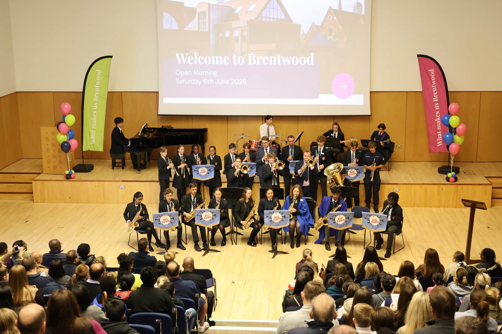 A school band performs on stage in front of an audience, with pupils playing various instruments. A large screen behind them reads Welcome to Brentwood, Open Morning, Saturday 6th June 2026—one of our exciting Open Events.