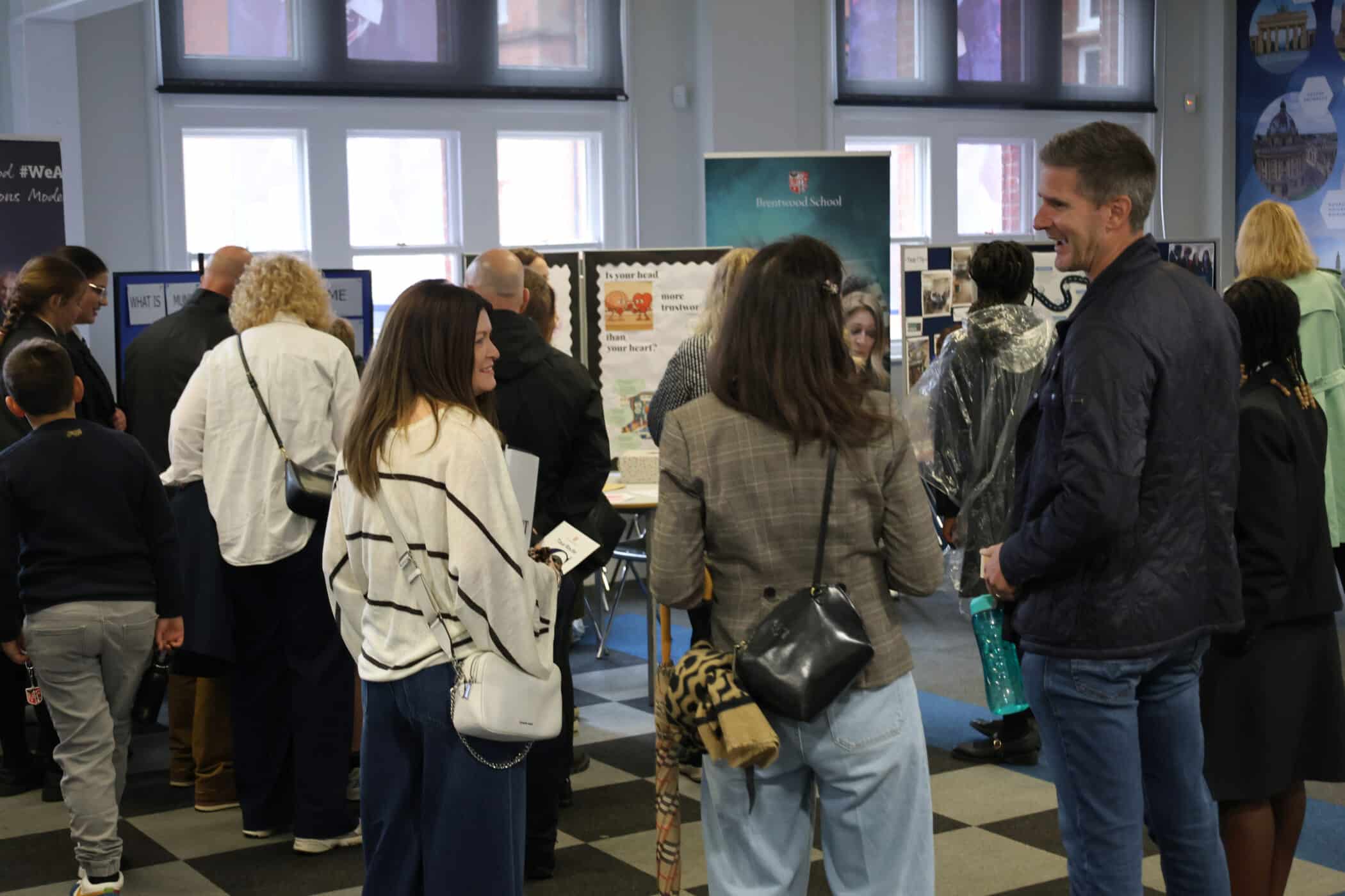 A group of adults and children stand indoors at Open Events, facing informational displays or posters. Some are talking, whilst others are looking at the displays. The atmosphere appears casual and sociable.