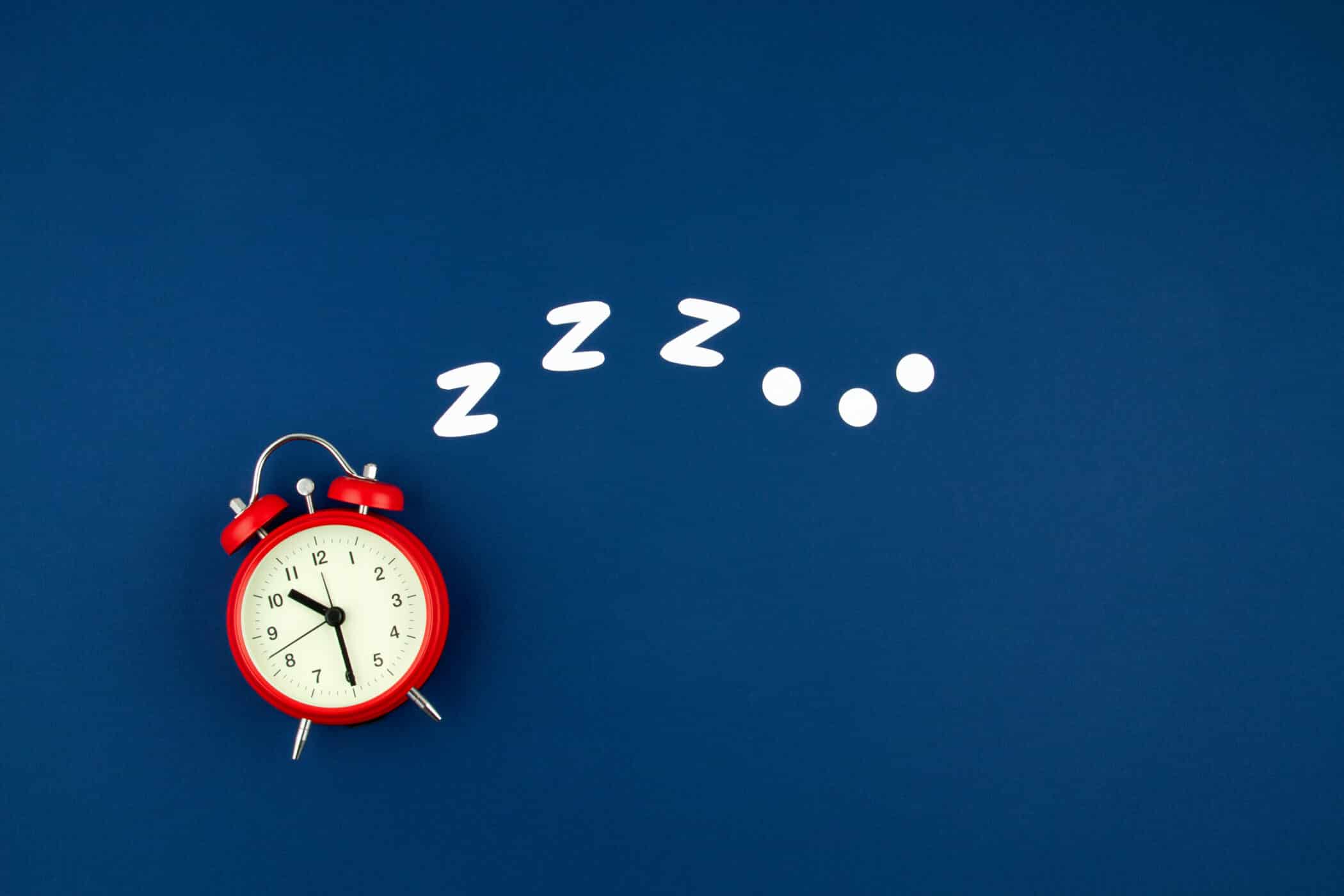 A red alarm clock on a blue background with white “Zzz” symbols above it, representing sleep or tiredness.