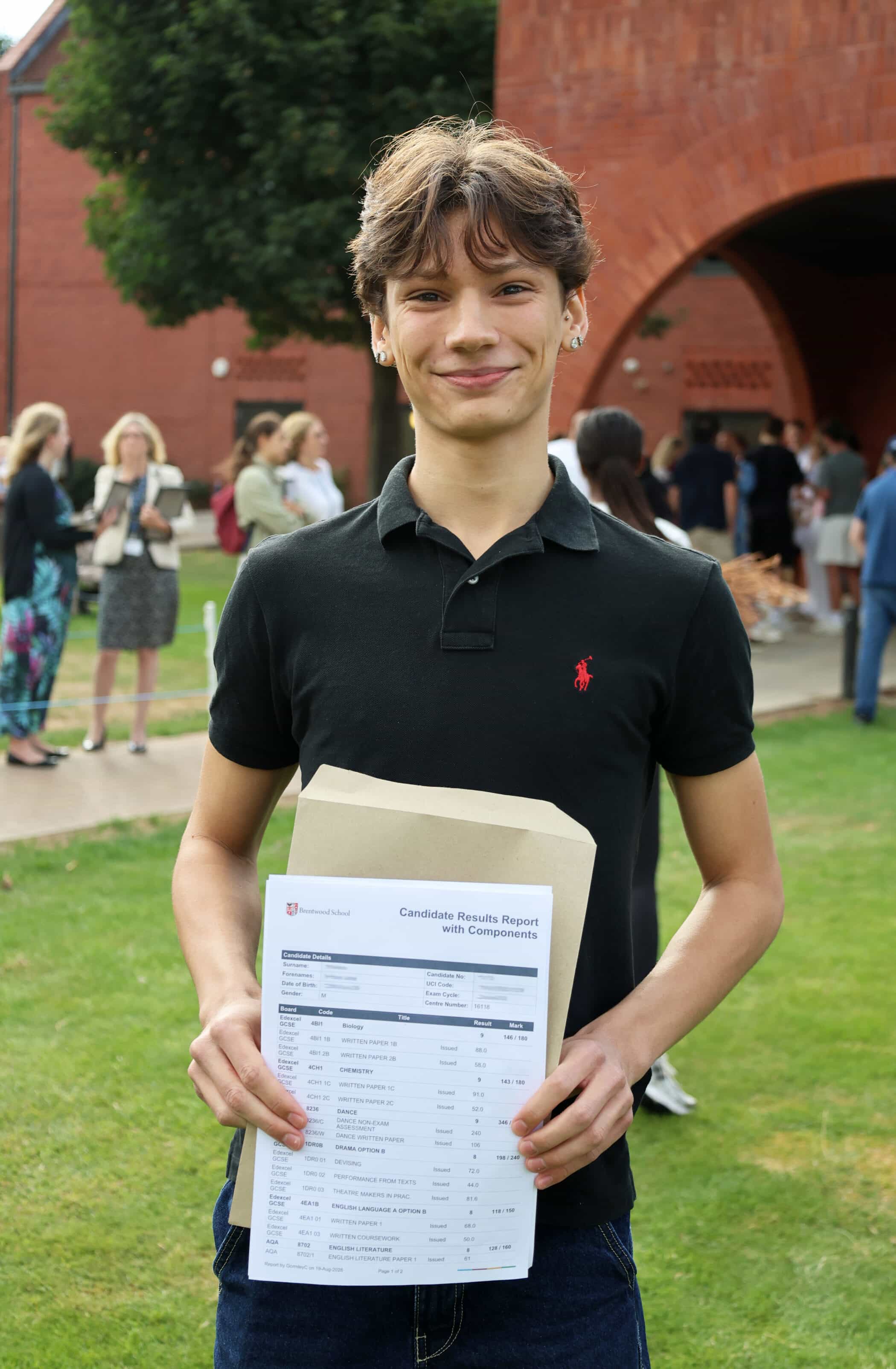 A smiling young person in a black polo shirt stands outside, proudly holding a GCSE candidate results report in front of them. People and a red brick building are visible in the background.