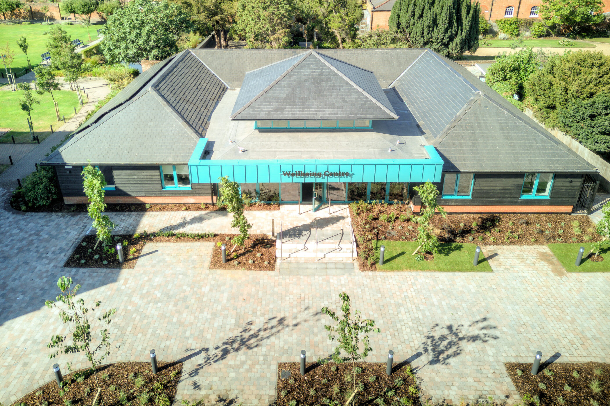 Aerial view of a modern building with a grey roof and teal entrance, labelled Wellbeing Centre, surrounded by landscaped gardens and pathways, showcasing the thoughtful design of the Wellbeing Centre.