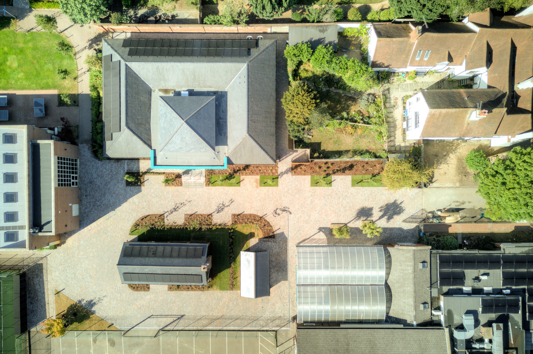 Aerial view of a courtyard with a central building, surrounding paths, gardens, and several adjacent structures, all bordered by trees and greenery, an ideal setting for the Wellbeing Centre.