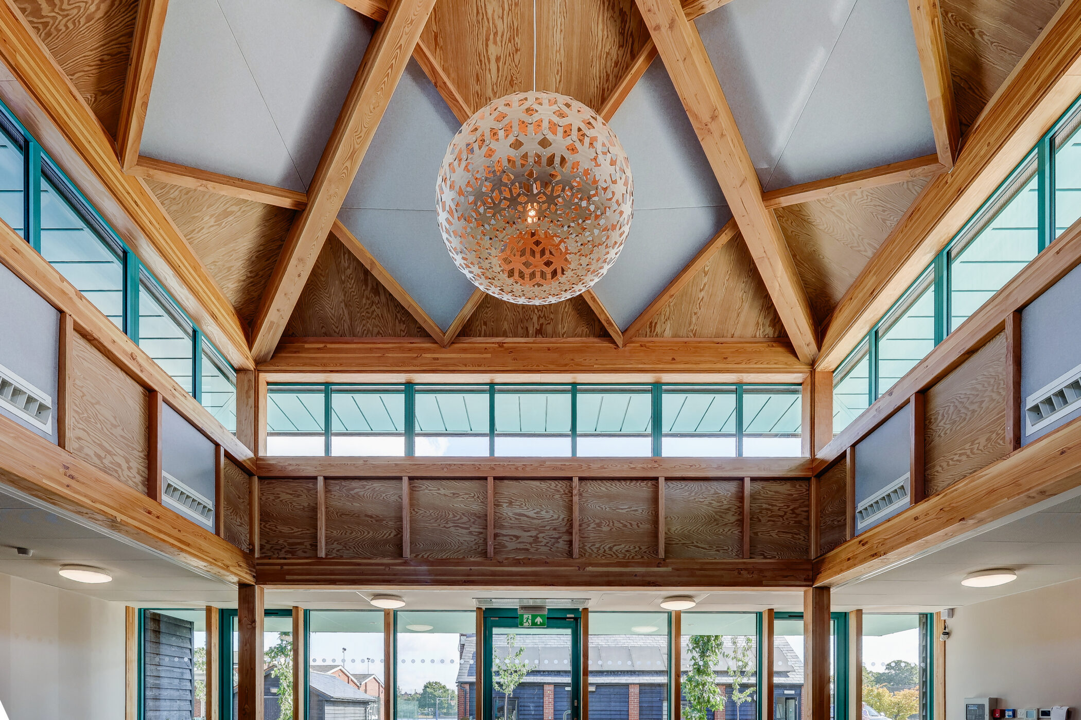 Spacious interior with wooden beams, large windows, and a decorative spherical chandelier hanging from a tall, pitched ceiling. Natural light fills the modern space, creating an inviting atmosphere ideal for a Wellbeing Centre.