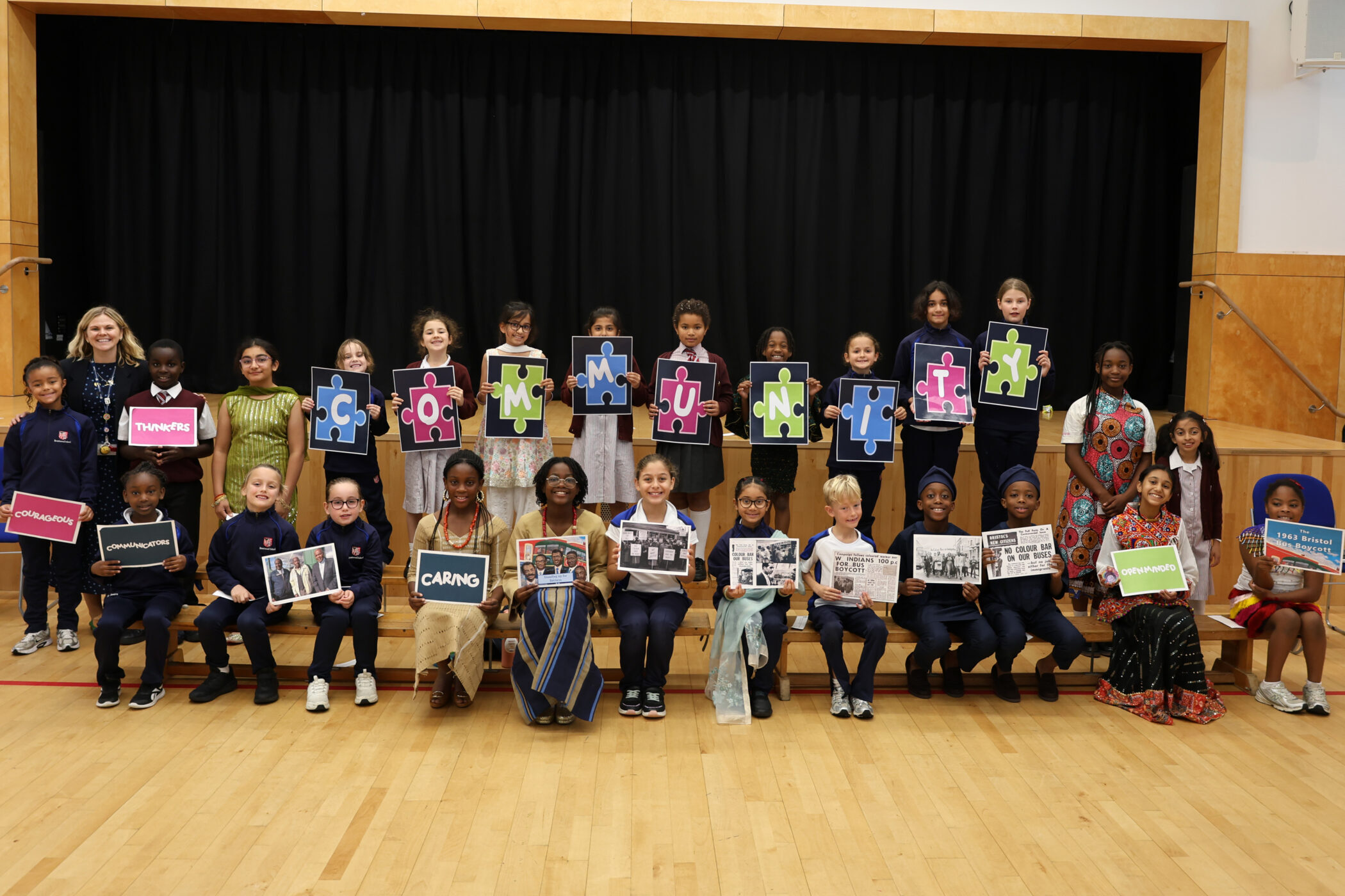 A group of students and teachers standing and sitting on a stage, holding jigsaw pieces that spell COMMUNITY and various historical photographs.