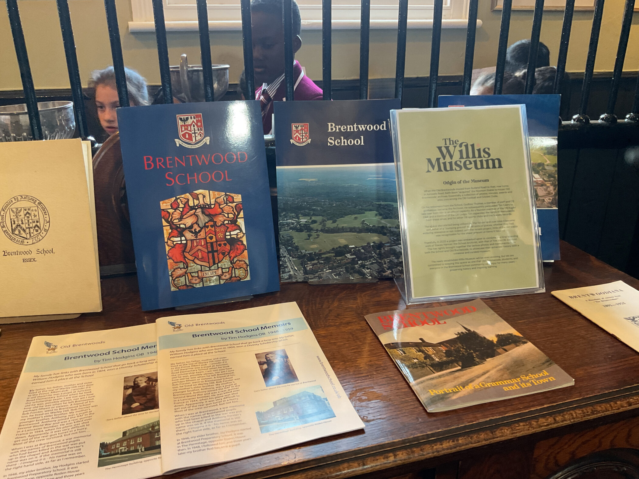 Display of Brentwood School and The Willis Museum books, pamphlets, and information cards on a wooden surface.