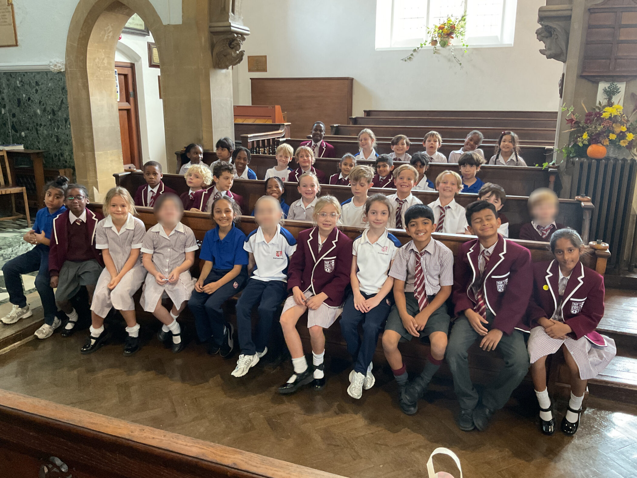 A large group of school children in uniforms sitting in rows of wooden pews inside a church.