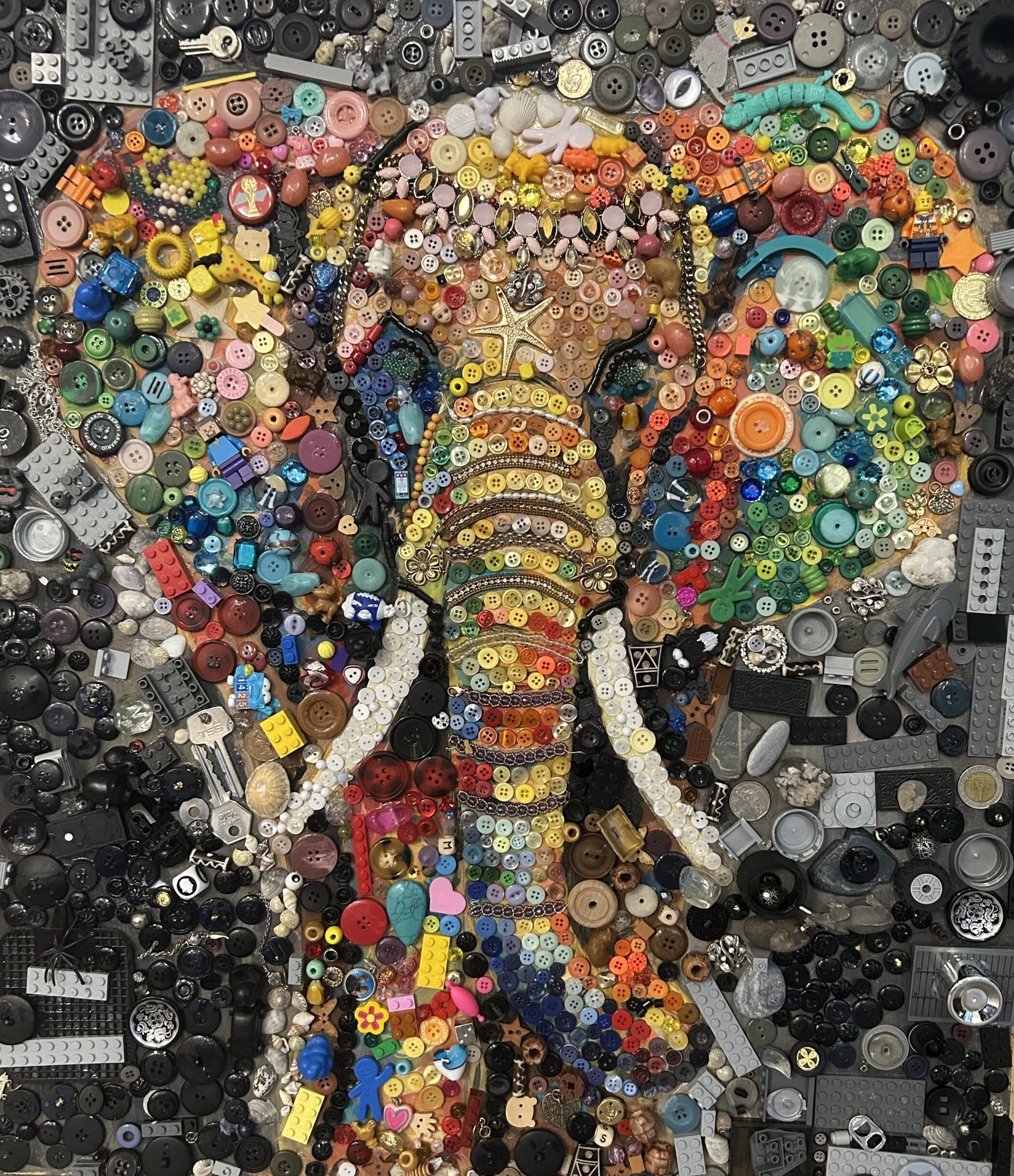 Mosaic of an elephant’s face created from a dense collage of colourful buttons, beads, plastic bricks, keys, and miscellaneous trinkets.