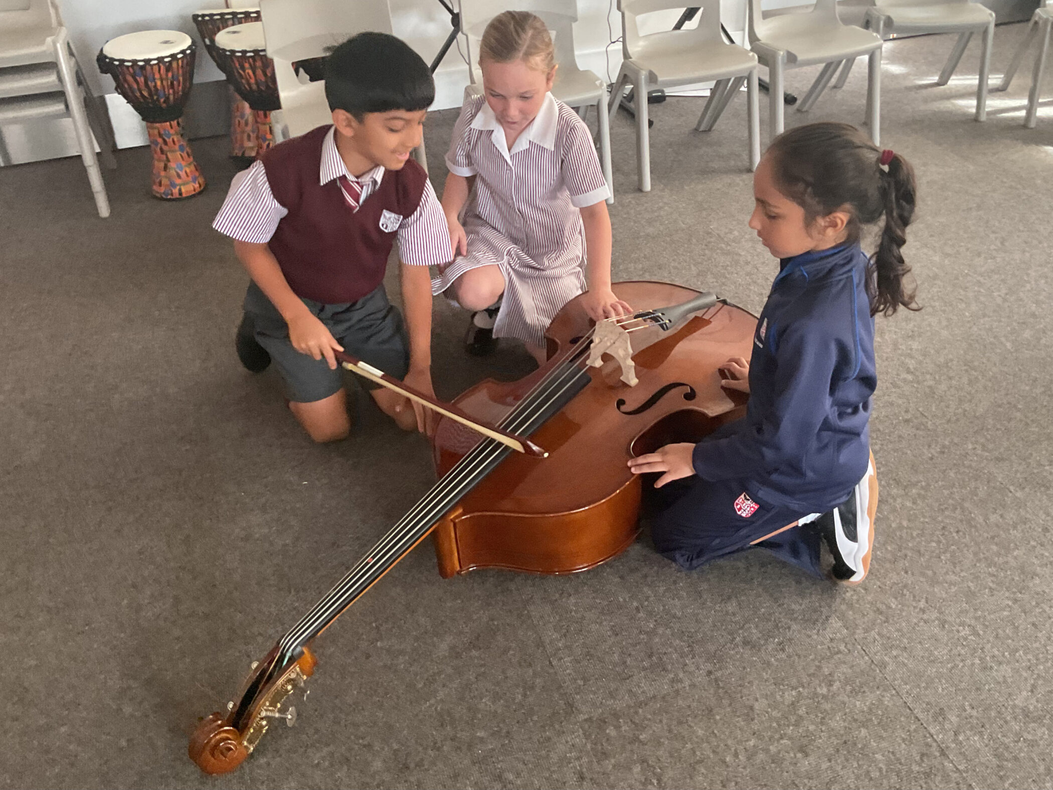 Three students kneeling on a floor, learning to play a double bass together.
