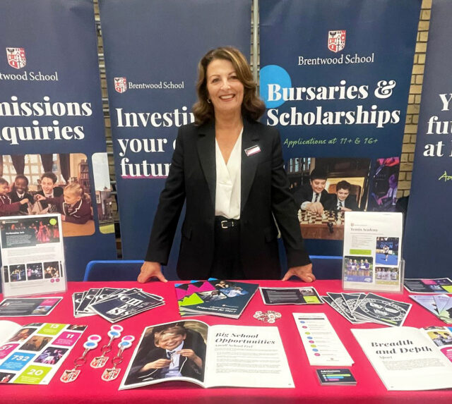 A woman stands behind a Brentwood School information stand with brochures explaining the admissions process spread across a red tablecloth.