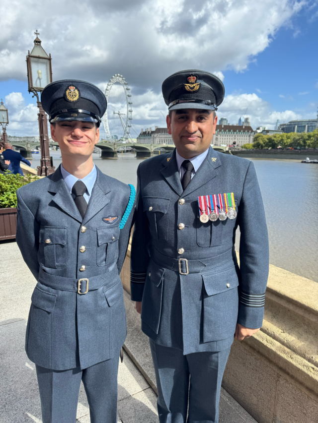 Two Royal Air Force officers in uniform standing by the River Thames with the London Eye in the background.